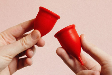 Zwei Hände vor rosa Hintergrund, die Menstruationstassen halten