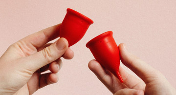 Zwei Hände vor rosa Hintergrund, die Menstruationstassen halten