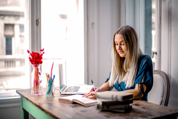 Home-Office: Frau sitzt am Schreibtisch und arbeitet am PC mit einem Buch