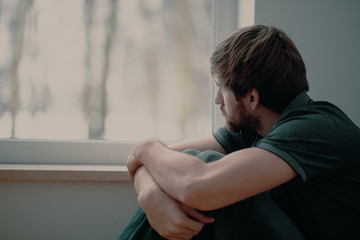 Mann sitzt vor Fenster und schaut traurig raus.