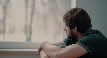 Mann sitzt vor Fenster und schaut traurig raus.