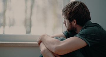 Mann sitzt vor Fenster und schaut traurig raus.
