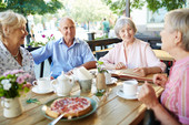 Senioren - ein Mann und dreit Frauen sitzen in einem Café am Tisch und unterhalten sich.