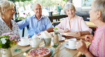 Senioren - ein Mann und dreit Frauen sitzen in einem Café am Tisch und unterhalten sich.